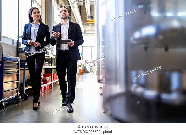 Businessman and businesswoman with tablet walking and talking in a factory