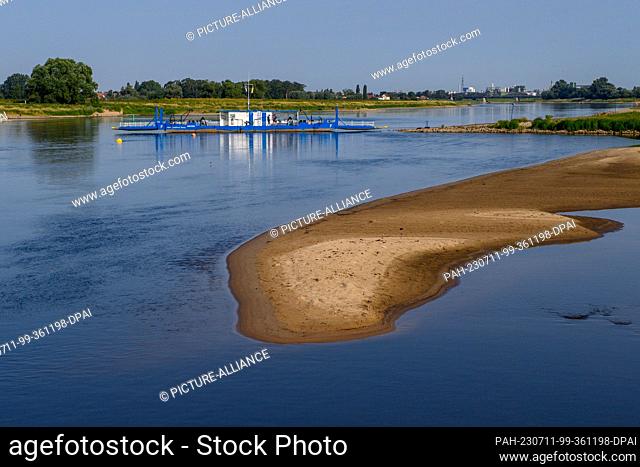 11 July 2023, Saxony-Anhalt, Magdeburg: A sandbank can be seen in the Elbe river. Behind it, the ""Saalhorn Barby ferry"" crosses over