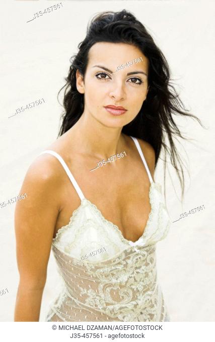 A young 20's, 30's woman wearing a lace white top, looks into camera with a pleased and sexy expression with her long black hair blowing in a breeze