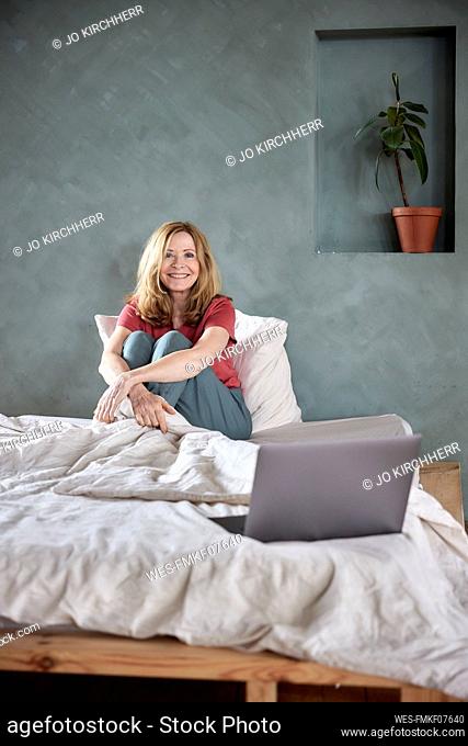 Happy woman sitting on bed in front of gray wall at home