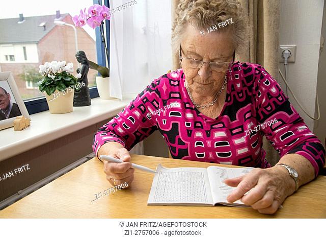 Old woman makes wordpuzzle at table in home for the aged