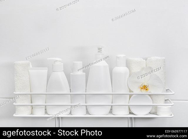 Close up white plastic bottles of cosmetic beauty care products and towels on bath shelf over white background, low angle view