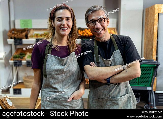 Smiling store owners wearing aprons standing in organic market