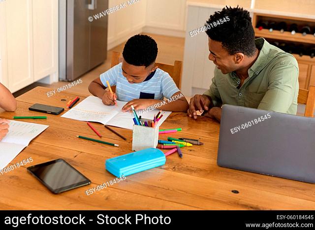 Happy african american father with daughter and son doing homework at home smiling