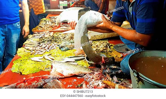 seller in fishmarket descaling Chitala fish with ramdao blade