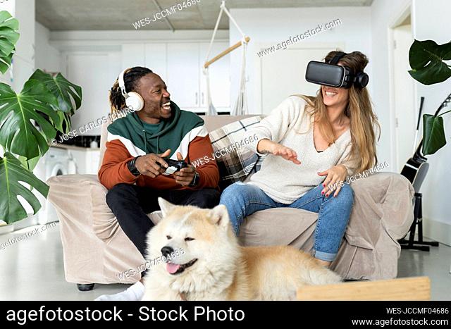 Cheerful couple playing video game in front of dog at home