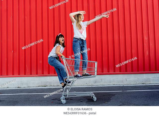 Sisters with shopping cart in front of red wall