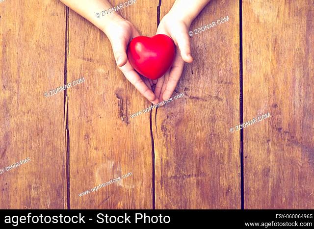 red heart in hands over vintage wooden background