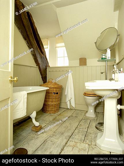 Rustic, country bathroom with wood wainscoting, whitewashed floorboards, an exposed wooden beam, and a sloping ceiling