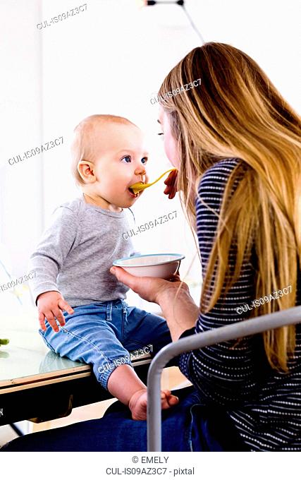 Mid adult woman feeding baby daughter on kitchen table