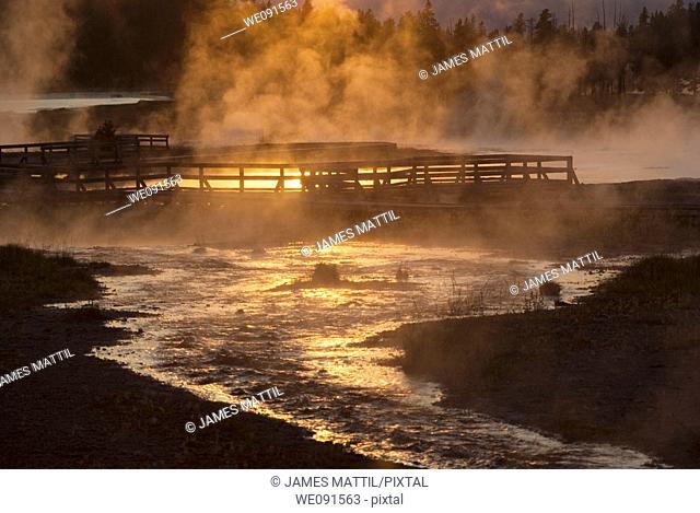 The setting sun reflecting on Firehole Lake geothermal area and boardwalk suggests a boiling pool of magma below