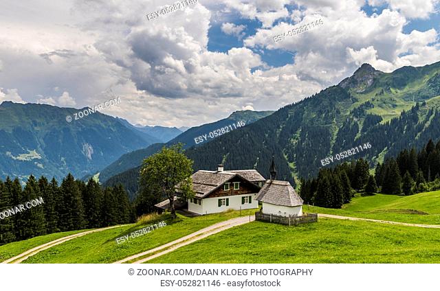 Old wooden cabin and chapel in Matschwitz with in the background the mountains of Montafon on a summers day, Austria