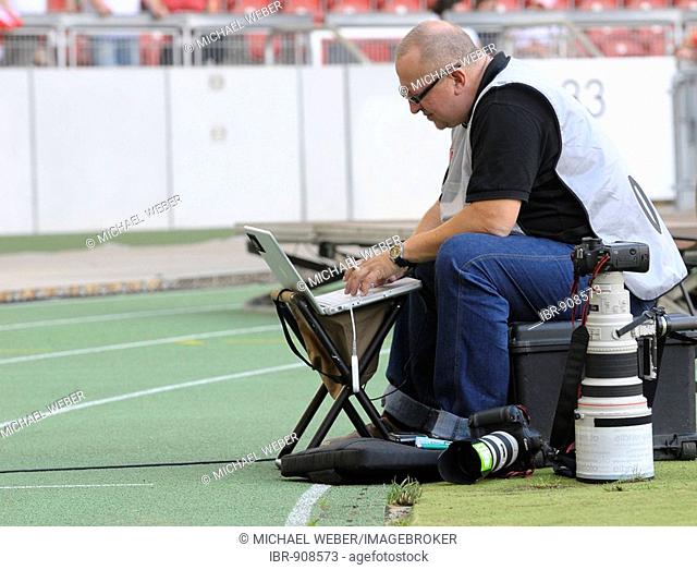 Press photographer in the stadium at the edge of the playing field working with Canon equipment and laptop