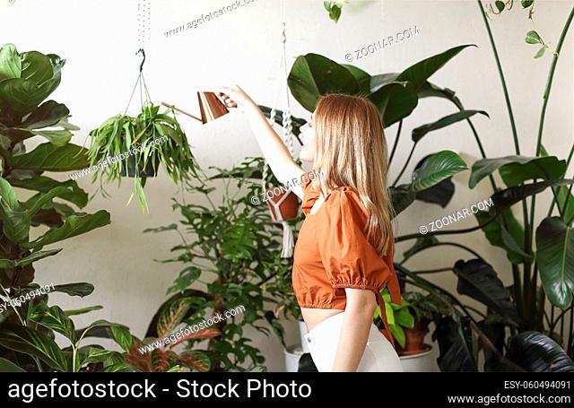 Young female with braids smiling and taking care of potted plants while gardening in weekend at home