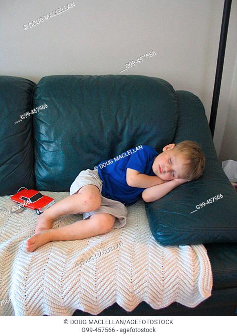 A three year old boy sleeps at home on a couch and with a little red car