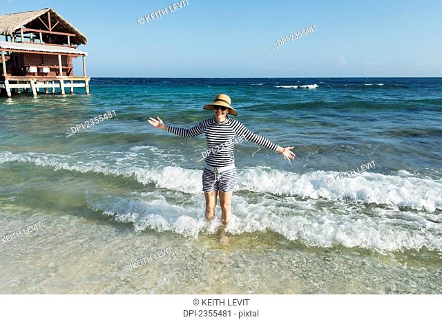 A Woman Stands In The Waves Beside A Hotel On The Coast; Utila, Bay Islands, Honduras