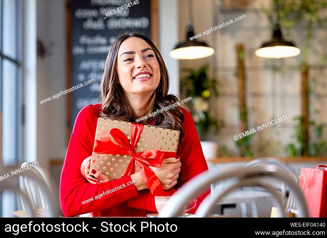 Smiling young woman with Christmas present sitting in cafe