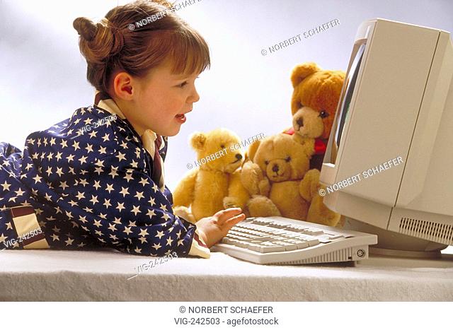 portrait, indoor, profile, 7-year-old girl wearing a blue pyjama with stars lies with her teddies in front of a computer writing  - GERMANY, 26/02/2005