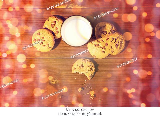 baking, eating, christmas, holidays and food concept - oat cookies and glass of milk on wooden table over lights