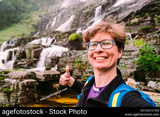 Woman tourist makes selfie photo on background of Tvindefossen or Tvinnefossen waterfall near Voss, Norway. Natural, landscape. Tvinde Camping