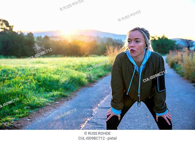 Young woman outdoors, taking a break from exercising, hands on knees