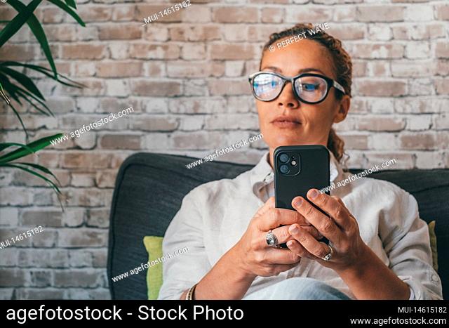 Thoughtful oung woman in casual clothes using mobile phone sitting on sofa in the living room of modern luxury apartment