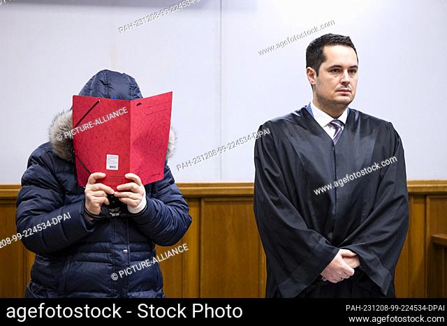 08 December 2023, Lower Saxony, Bückeburg: The defendant (l) stands in a courtroom in Bückeburg district court before the start of the trial and holds a folder...