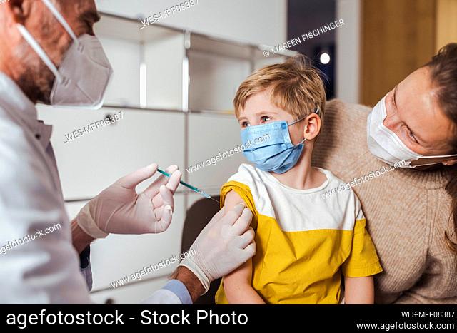 Boy looking at doctor holding vaccine injection in center