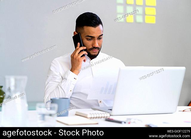 Serious businessman looking at strategy while talking on smart phone at office