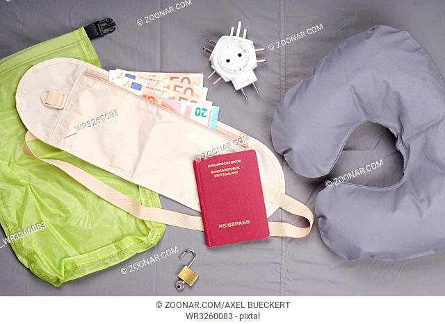 themed flat lay with travel pillow, money belt, german passport, international travel adapter and padlock