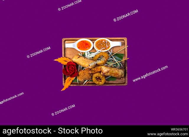 Mixed plate with thai food with purple background and copy space. Plate made out of wood and spring rolls