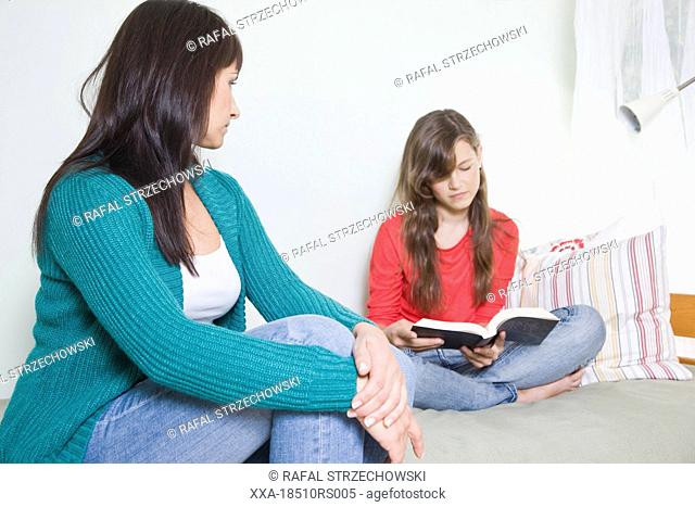 mother looking at daughter reading a book