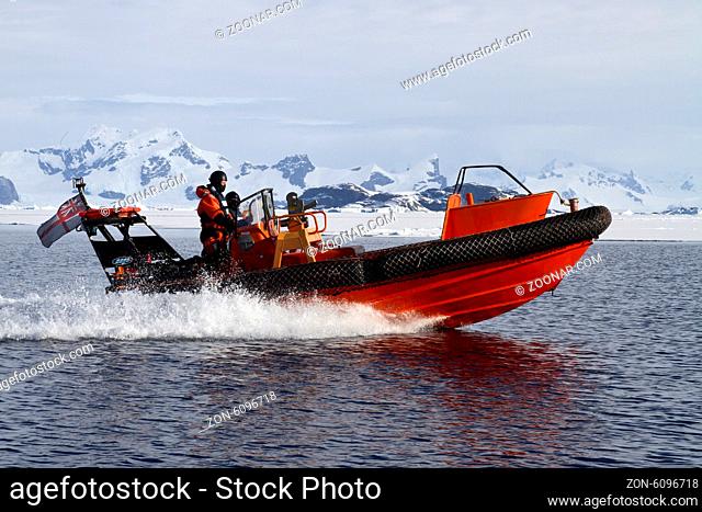 orange boat sailing at high speed in Antarctic waters against mountains