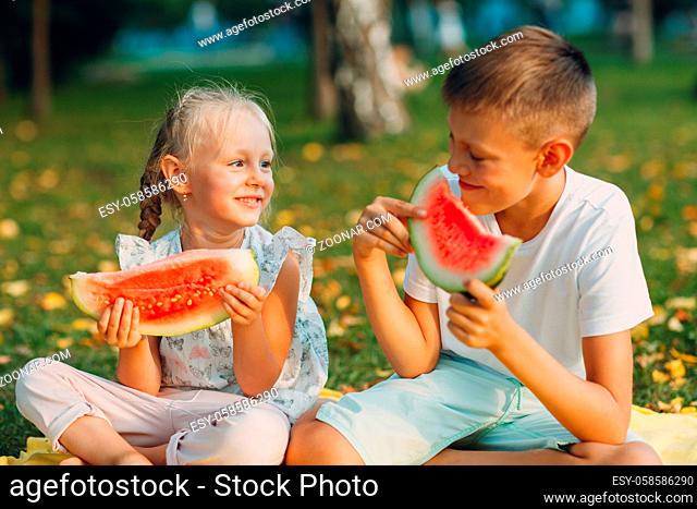 To cute kids lttle boy and girl eating juicy watermelon in the picnic at autumn park meadow