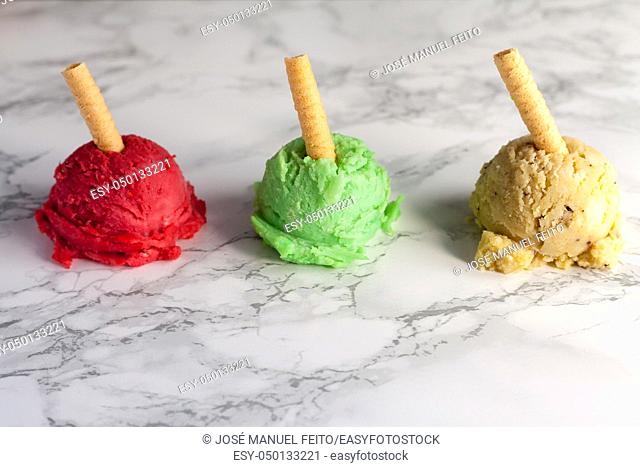 three ice cream balls green, yellow and strawberry colour with wafer on marble table background
