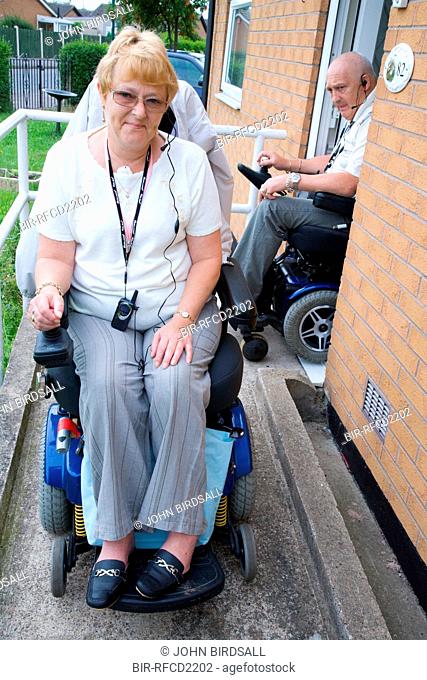 Disabled couple leaving their house down a concrete wheelchair ramp