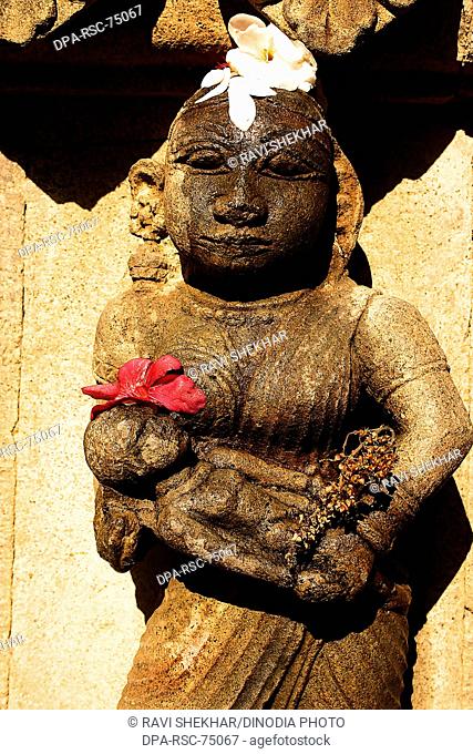 Indian mother and child , carved on wall of Ahilayabai temple , with red flowers for  worshiping in Hindu religious tradition , ornamental carving on stone