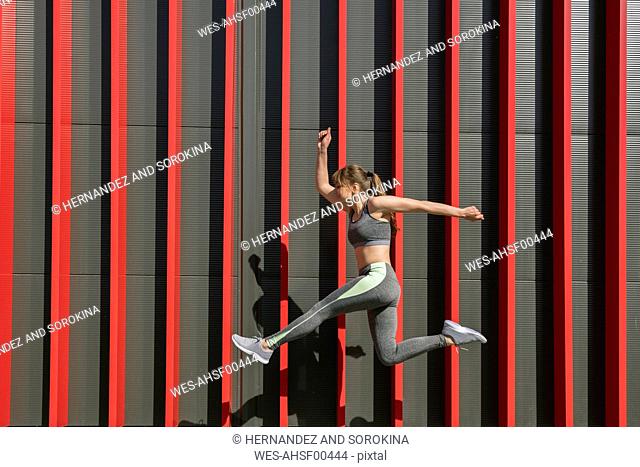 Sportswoman jumping in front of a red wall