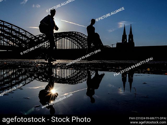 24 October 2023, North Rhine-Westphalia, Cologne: Two men walk along the banks of the Rhine in the evening sun after a rainy day