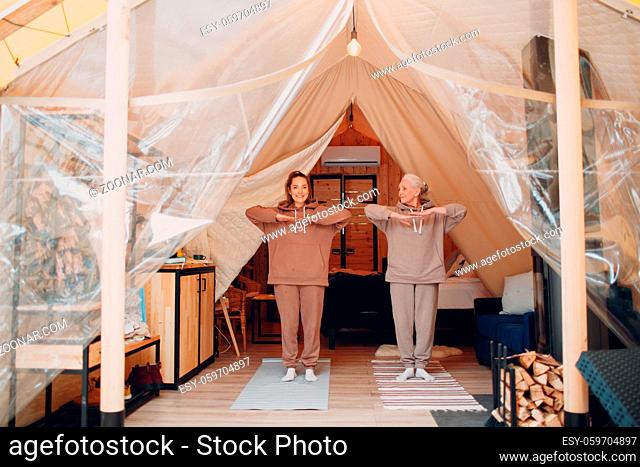Family doing exercises sports indoors. Young and senior elderly woman relaxing at glamping camping tent. Mother and daughter modern vacation lifestyle concept