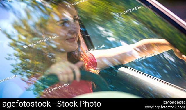 Motion blured image of happy young woman driving a car on a summer road trip travel vacations. Shot trough windshield