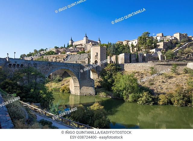 Shot from green water river Tagus, Tajo in Spanish, of Alcantara arch bridge and door, landmark and monument from ancient Roman age, in Toledo city, Spain