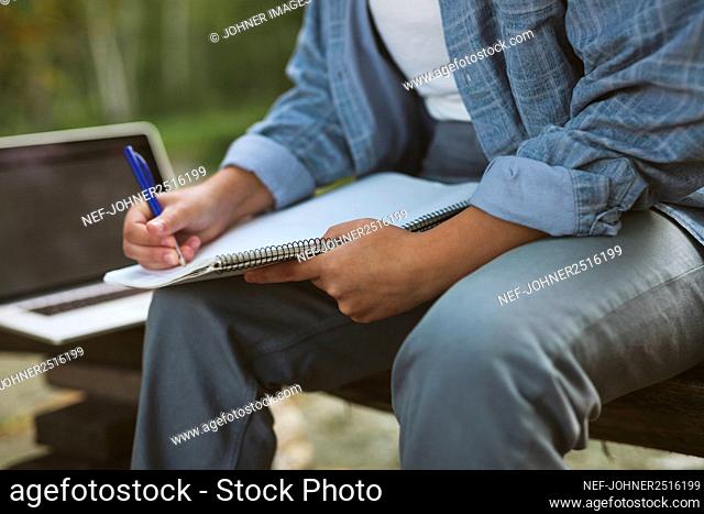 Young woman with notepad and laptop sitting on bench