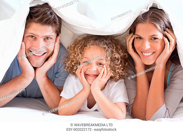 Family posing under a duvet while looking at the camera