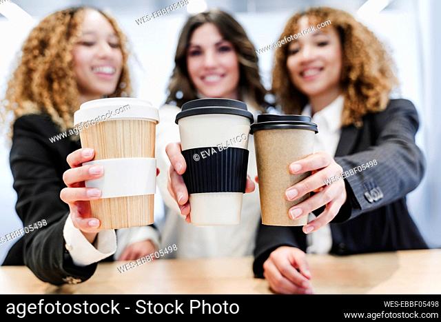 Business colleagues holding disposable coffee cups at coworking office