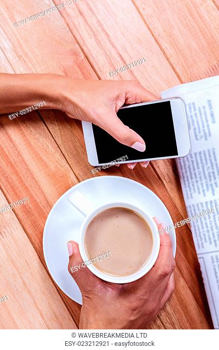 Part of hands holding coffee and smartphone on wooden desk