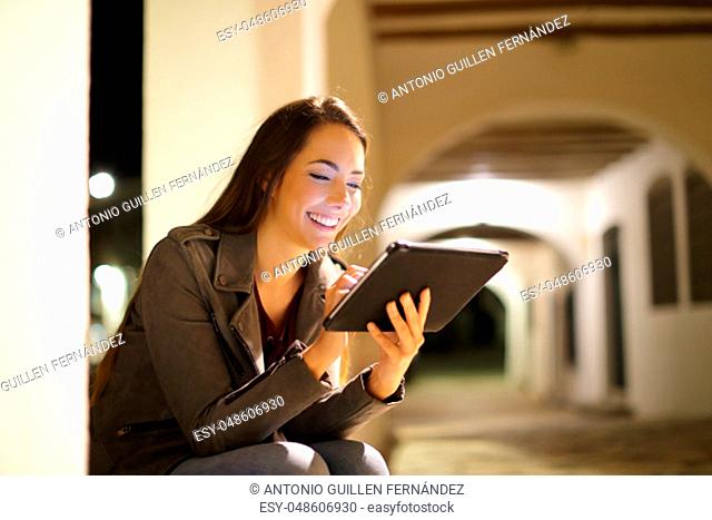 Happy lady browsing tablet content sitting in the night in the street