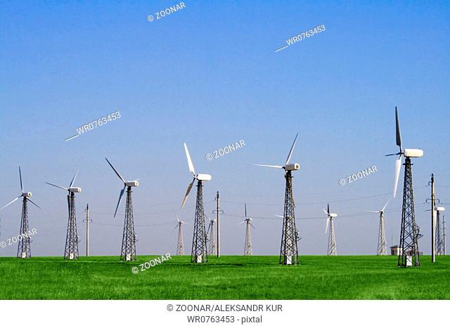 Wind farm turbines in green field over blue sky
