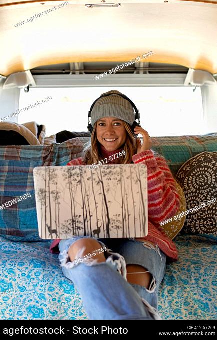Retrato feliz joven con auriculares y portátil en autocaravana