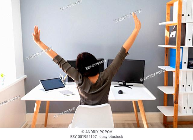 Rear View Of Young Businesswoman Stretching Her Arms In Office